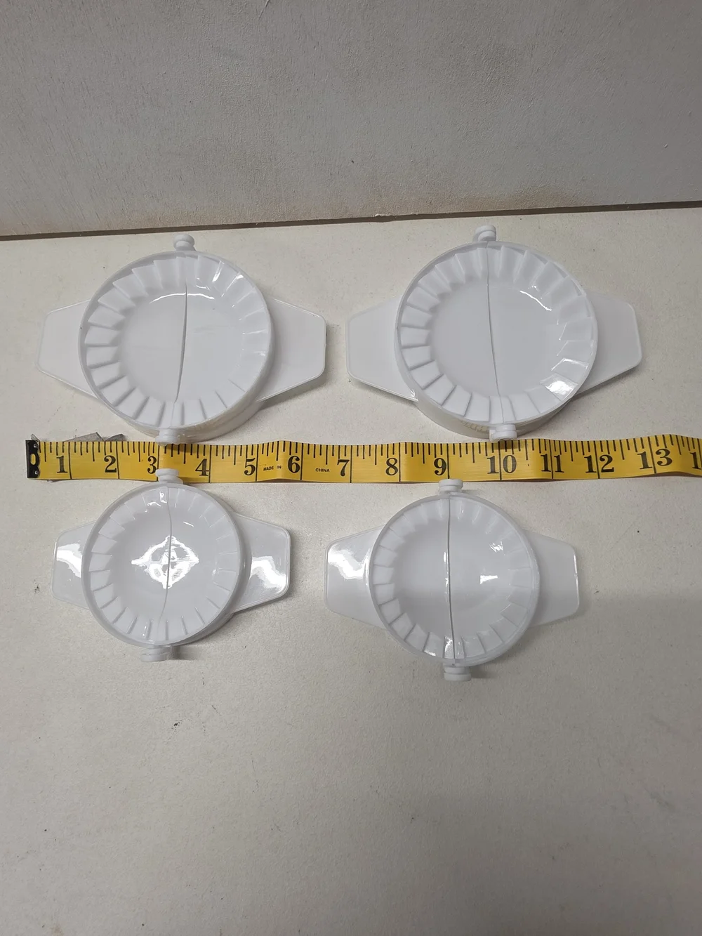 Set of 4 white plastic dumpling/empanada presses in two different sizes.
